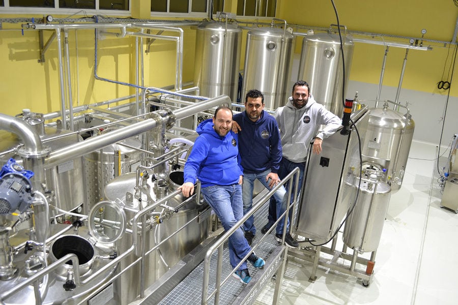 three men smiling happily at the camera at 'Siris Microbrewery' plant